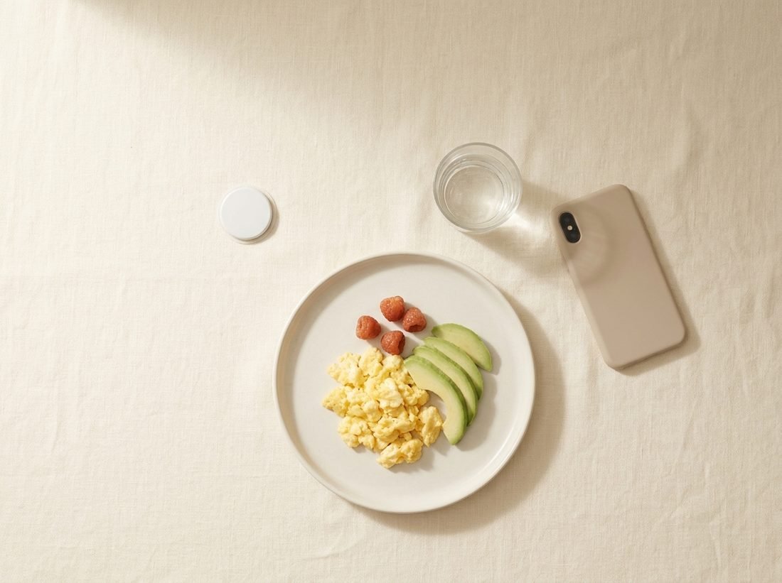 Overhead view of a simple breakfast, a glass of water, a phone and a small circular biosensor on a linen surface